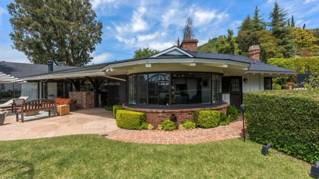 Exterior view of the Gene Wilder House featuring charming vintage architecture, lush greenery, and a warm nostalgic atmosphere in a quiet residential neighborhood.