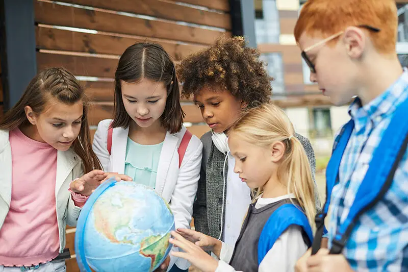 Children examining a globe together in an outdoor setting with wooden backdrop