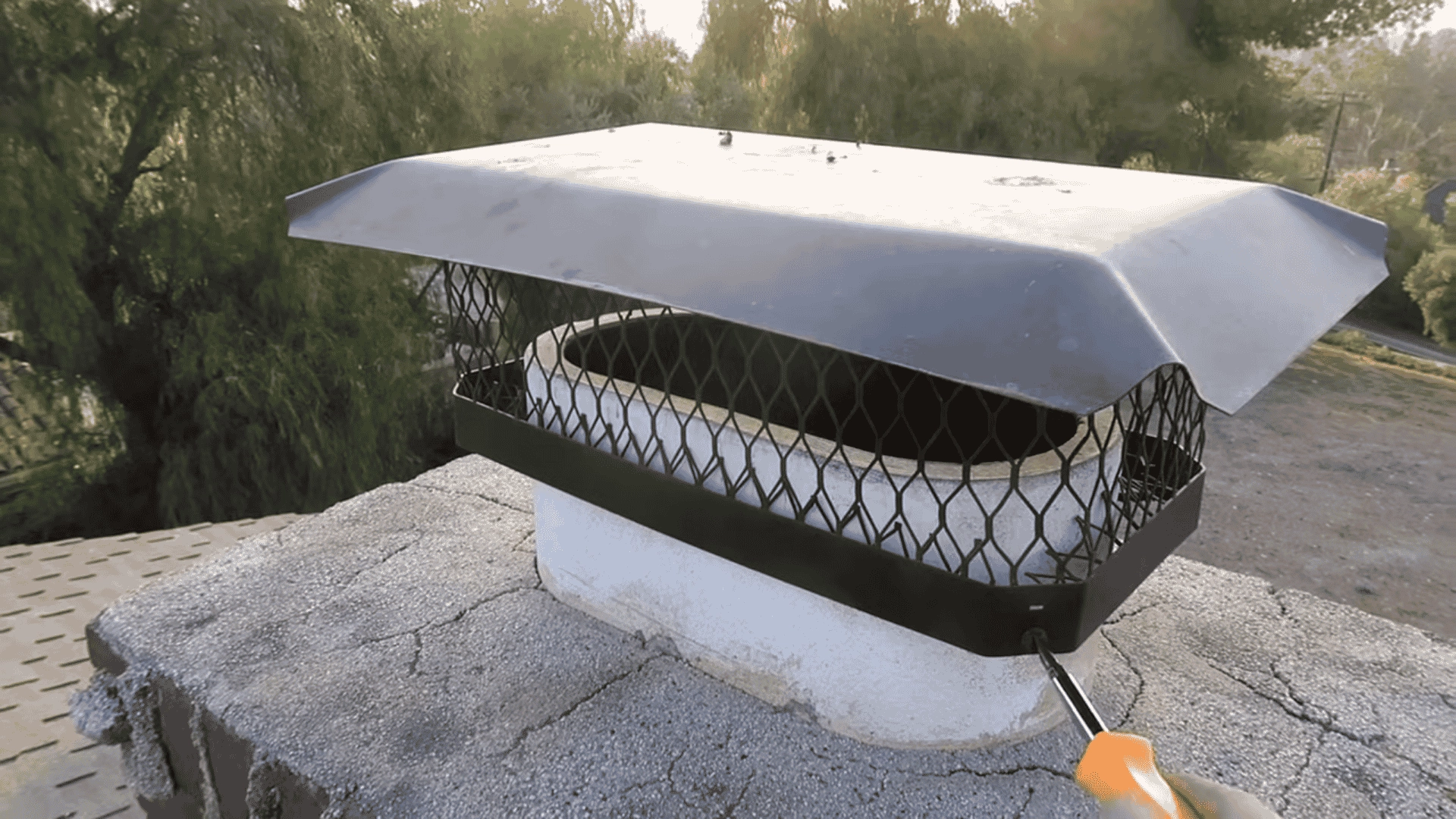hand-using-a-screwdriver-to-detach-a-black-metal-cap-from-a-brick-chimney-flue