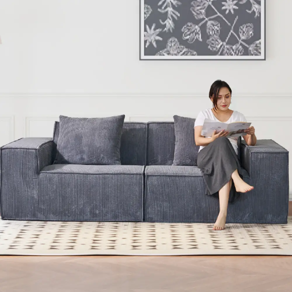 Woman reading on gray sofa in minimalist living room with patterned rug and floral artwork