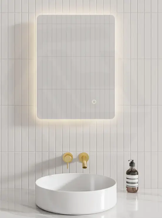 Round white basin with gold fixtures under illuminated mirror on tiled bathroom wall