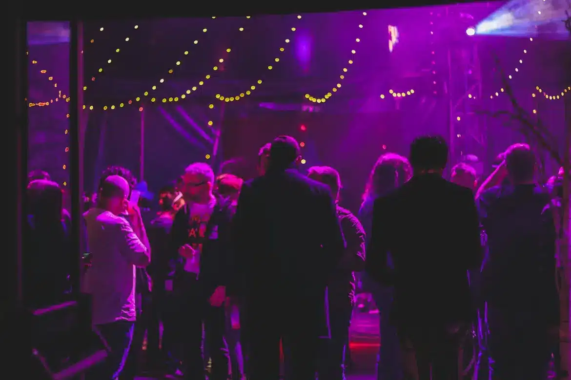 People mingling at an indoor party with purple lighting and string lights overhead