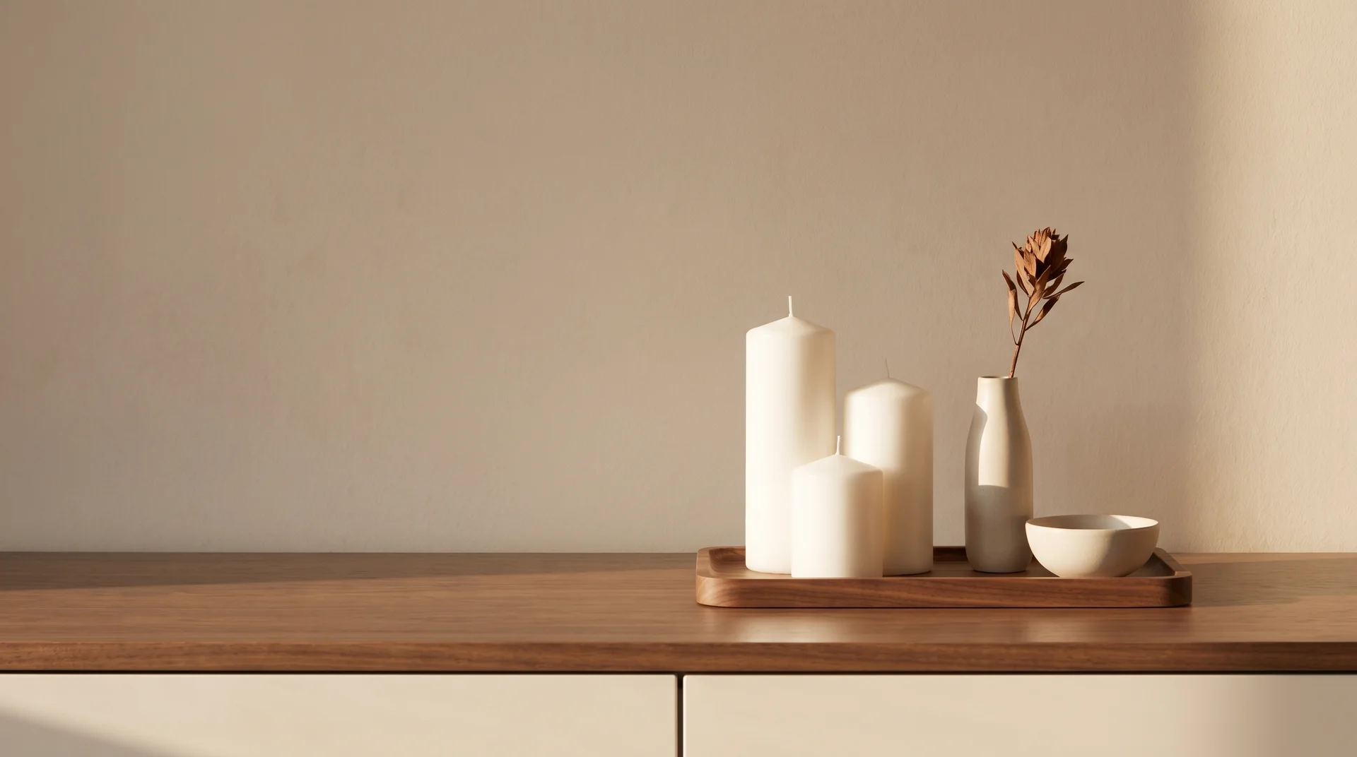 A wooden tabletop tray holding three white pillar candles, a small vase with a single dried flower, and a white ceramic bowl.