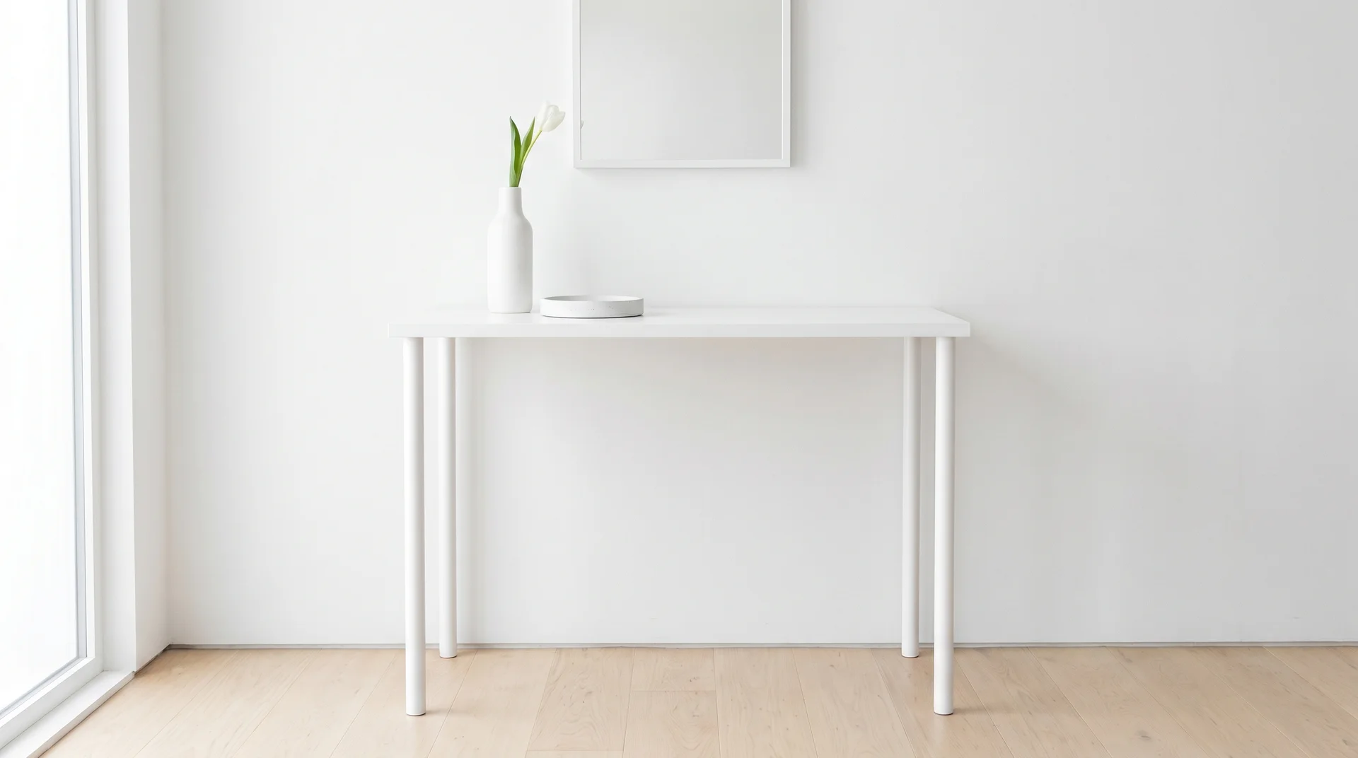 Simple white minimalist console table against a plain white wall styled with a single flower in a slender vase.