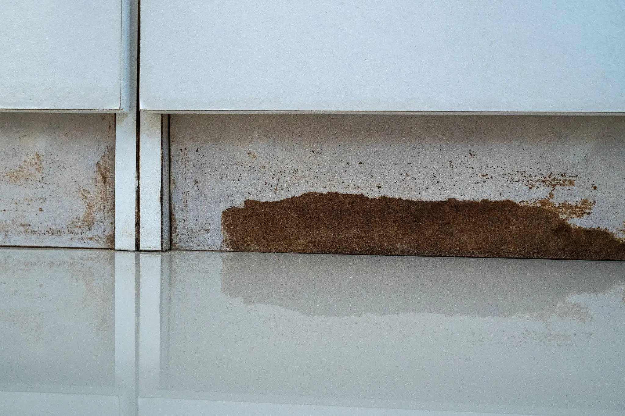 Dirty wall with rust and mold stains above a reflective glossy surface