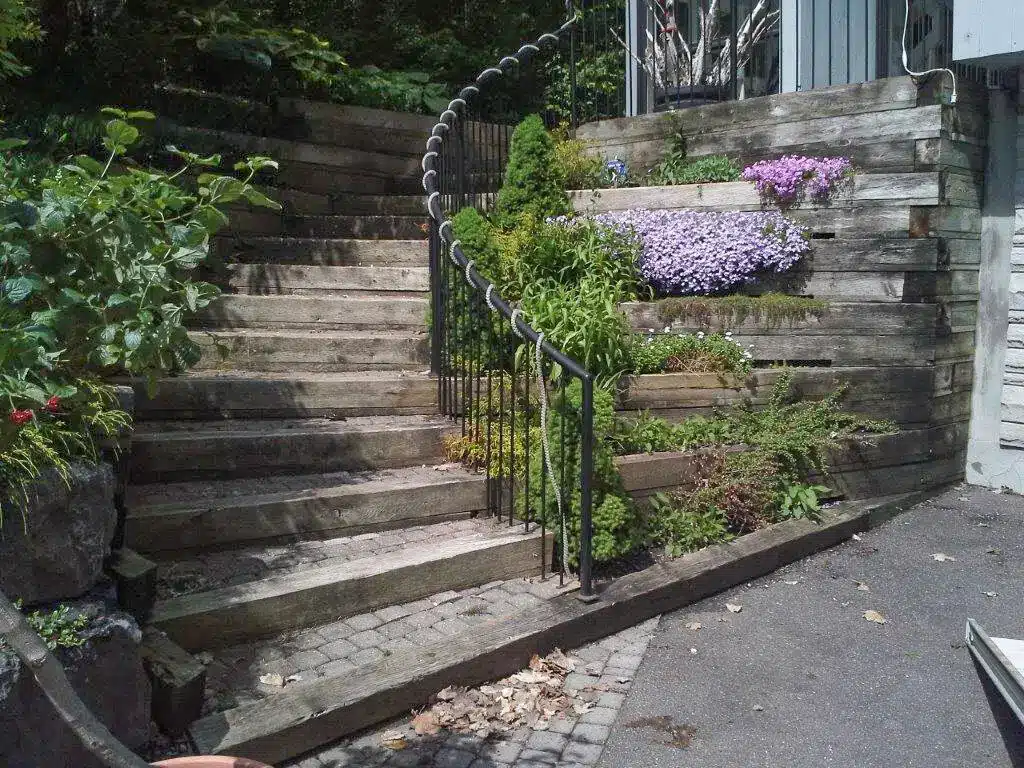 Wooden outdoor stairs with metal railing surrounded by lush greenery and purple flowers