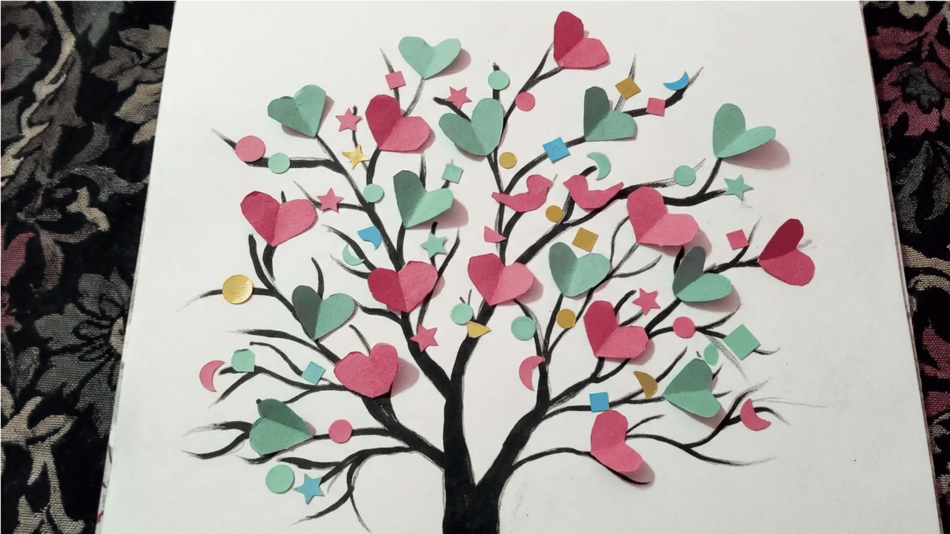 Paper heart tree craft with colorful folded hearts and decorative cutout shapes on black branches.