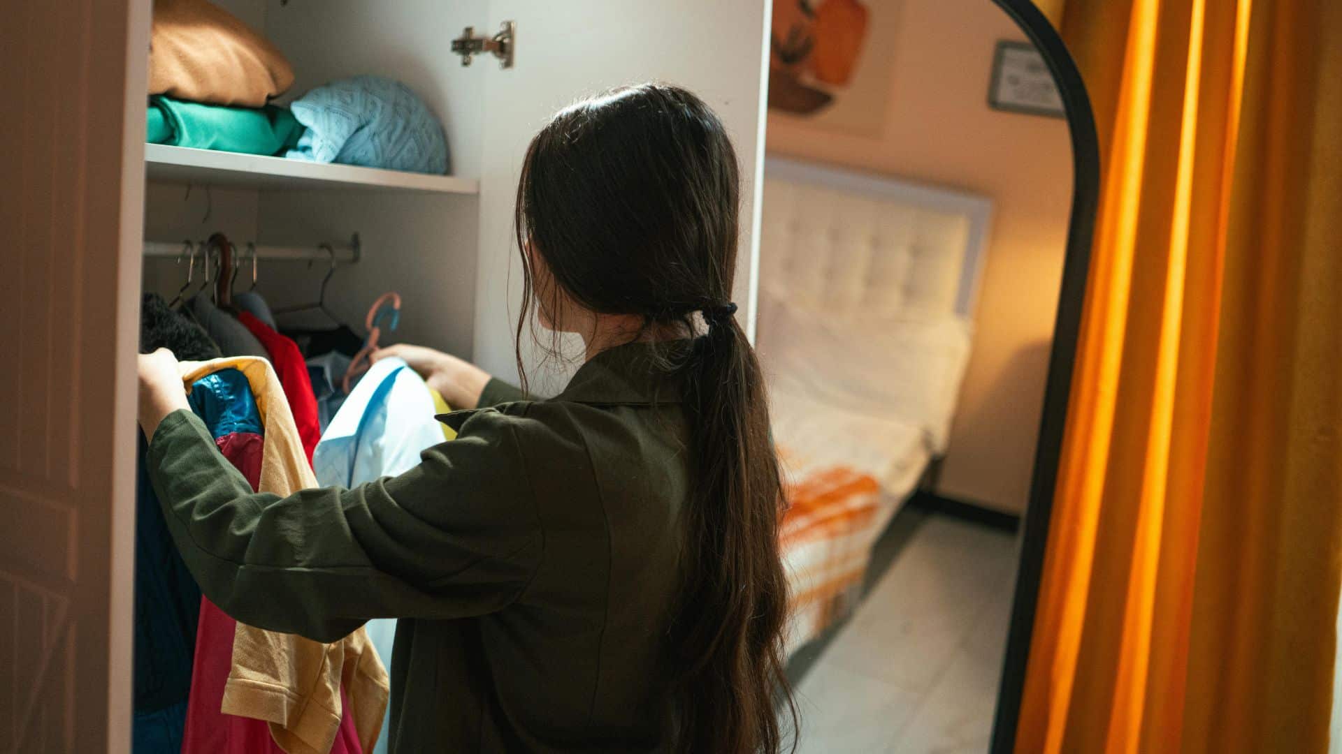 Person arranging clothes in wardrobe, showing how to organize your room efficiently with neat storage, decluttering, and better space use