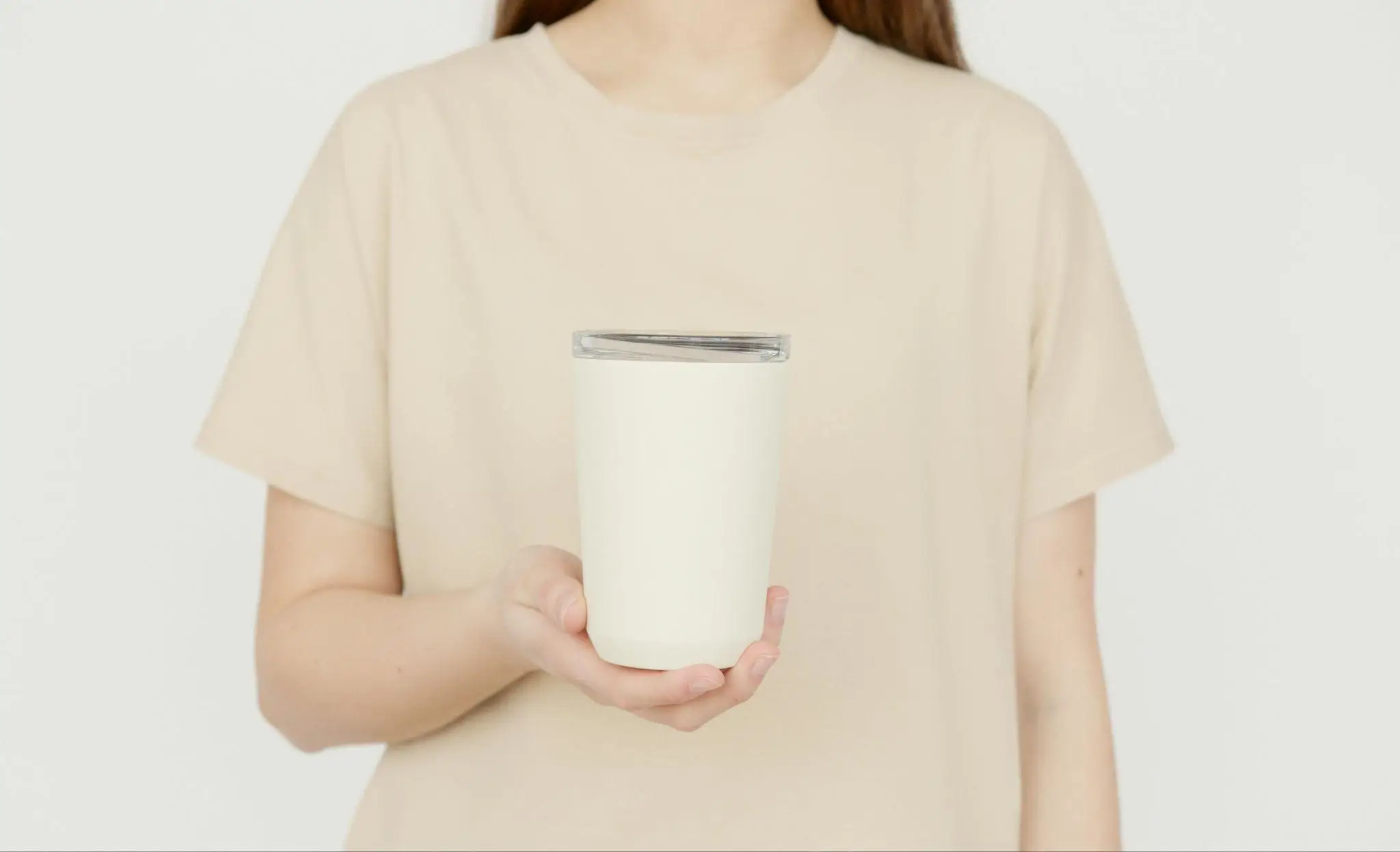 Person holding a white travel tumbler in a neutral-toned indoor setting