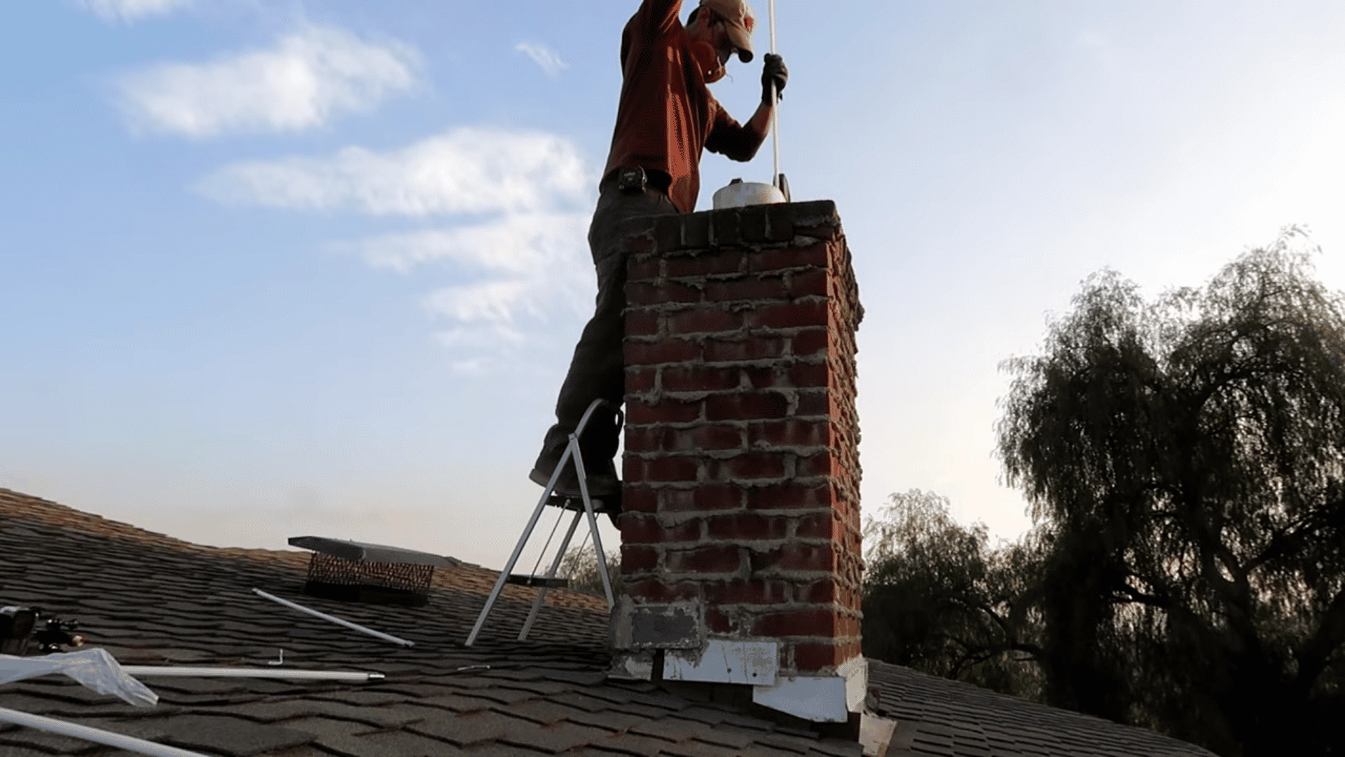 person-on-a-roof-ladder-using-a-long-rod-to-sweep-the-interior-of-a-brick-chimney