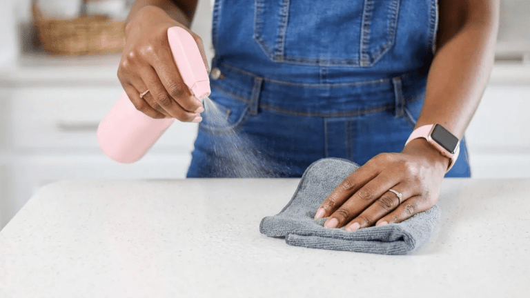 Person spraying a gentle cleaner onto a white quartz countertop while wiping the surface with a soft microfiber cloth for streak-free cleaning.