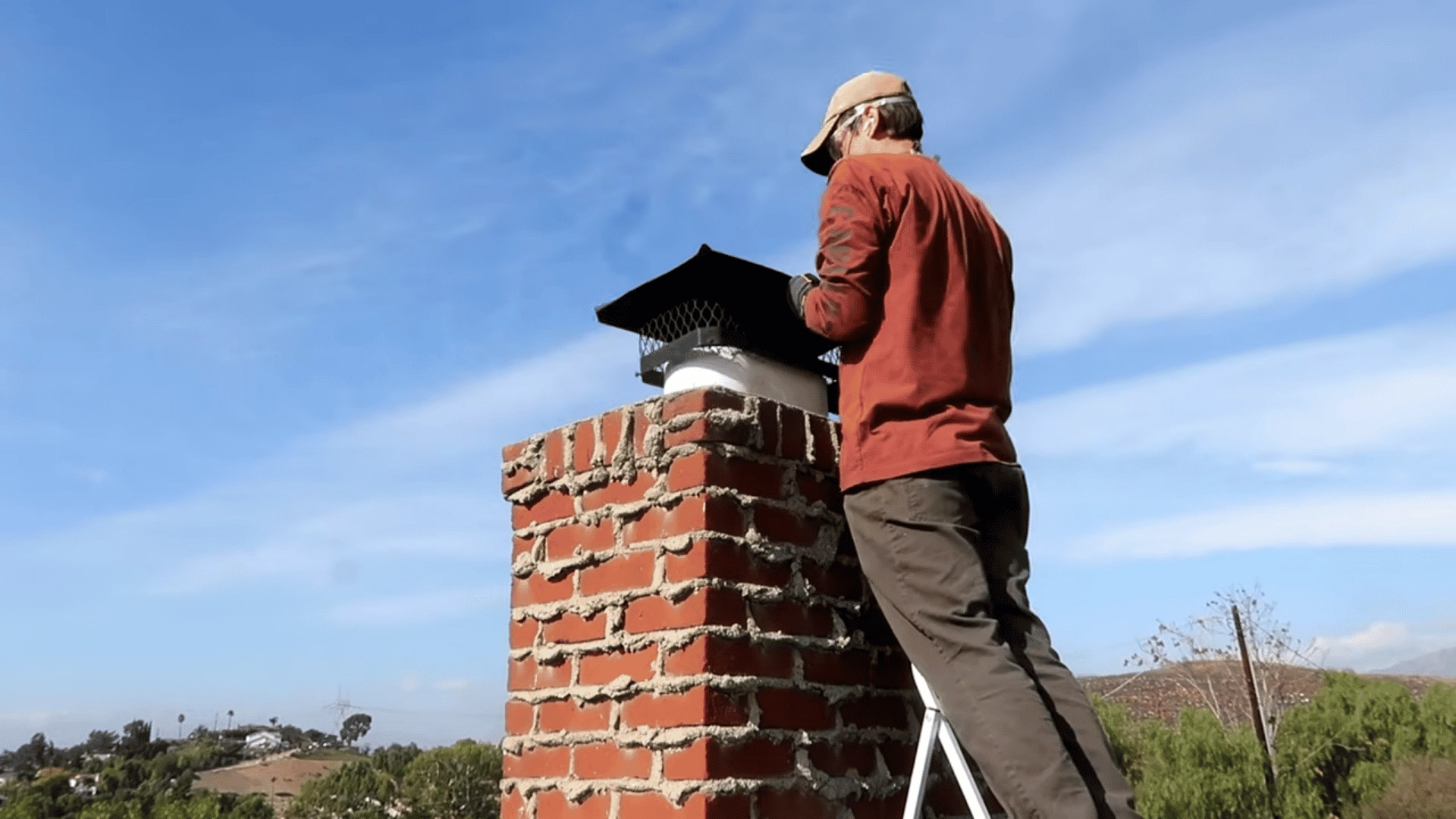 person-standing-on-a-ladder-next-to-a-chimney-reinstalling-the-black-metal-spark-arrestor
