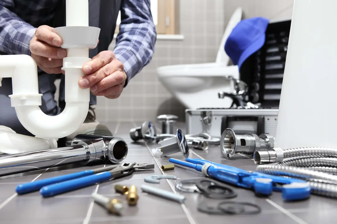 Plumber assembling pipes in bathroom with scattered tools on tiled floor