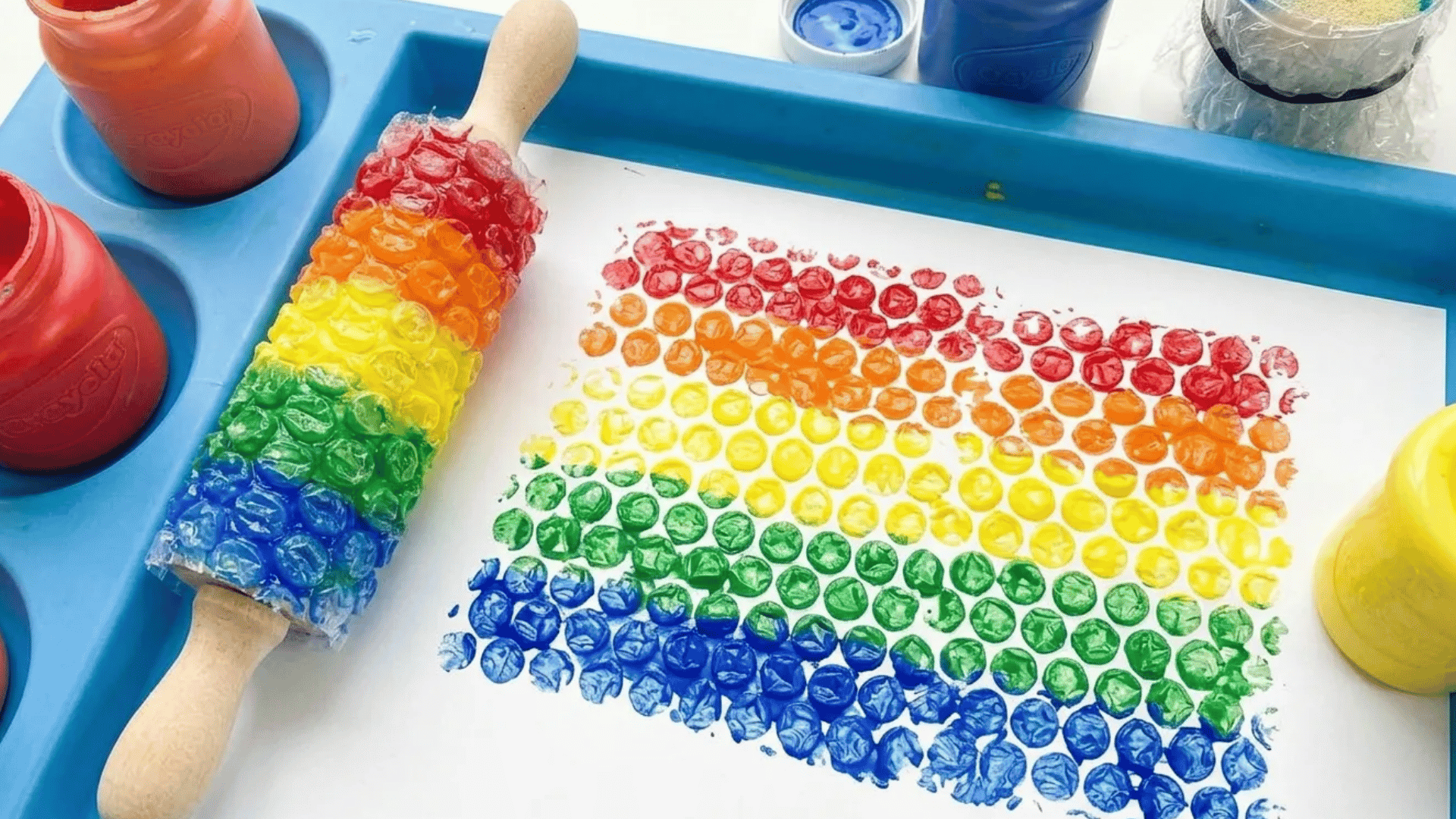 Rainbow bubble wrap painting activity using colorful paint and a rolling pin on white paper.