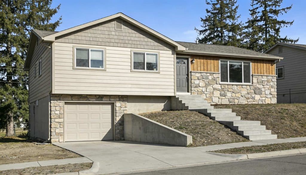 A two-story raised ranch house with a stone and light beige siding exterior, an integrated garage, and concrete steps leading to the front door.