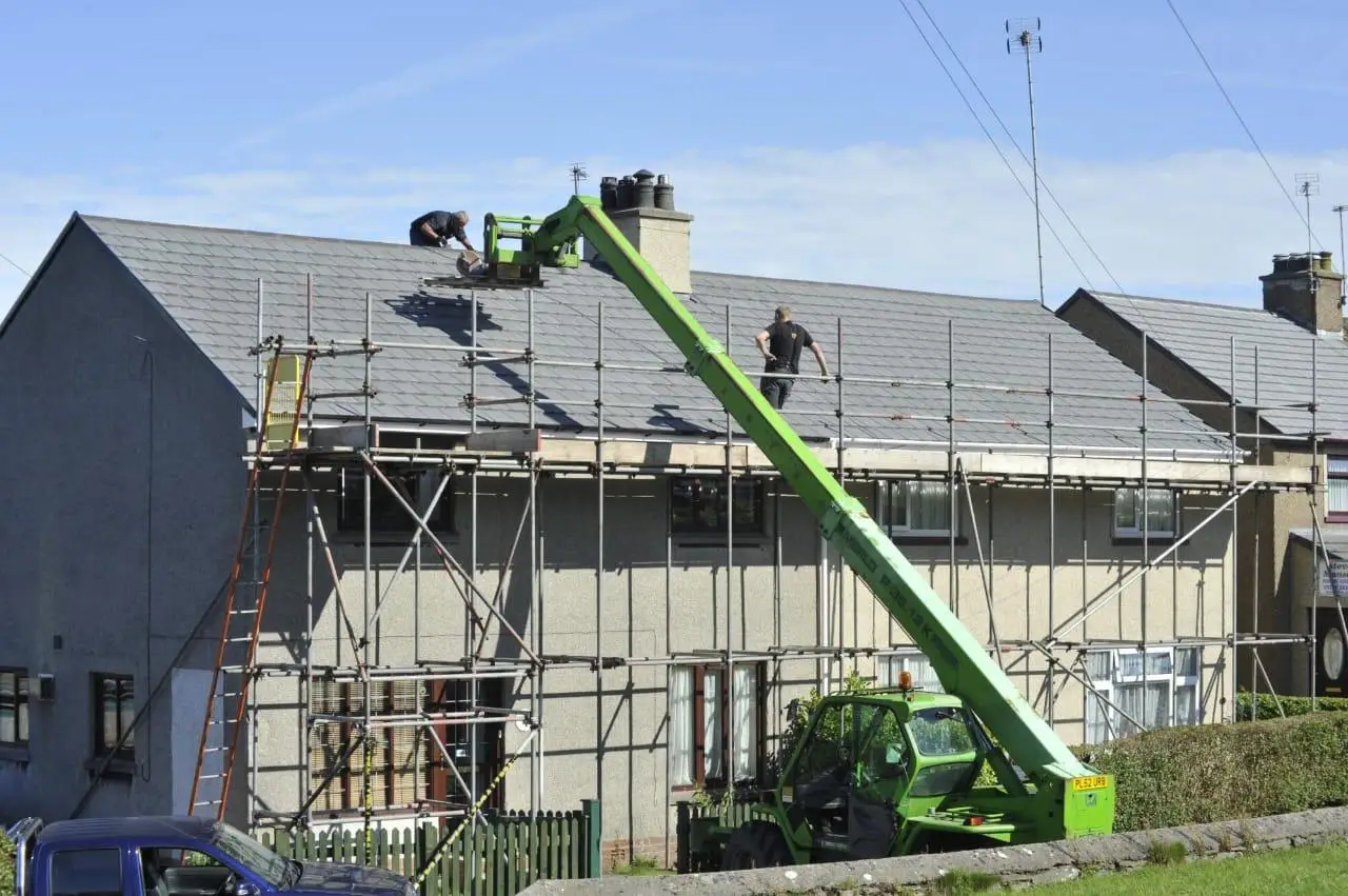 Construction workers repairing roof on residential building with scaffolding and green lift equipment