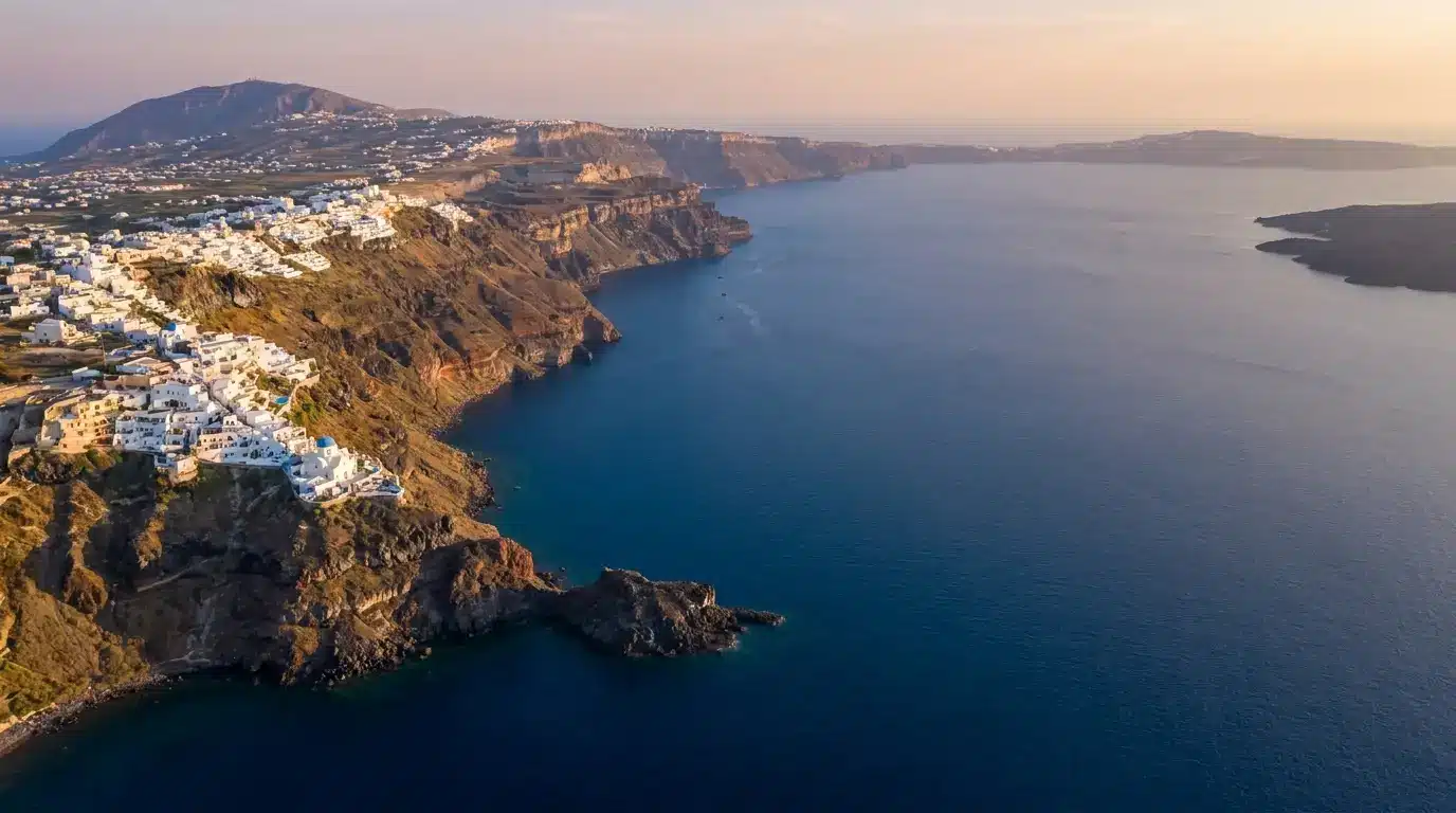 Coastal cliffside village with white buildings overlooking calm blue sea at sunset
