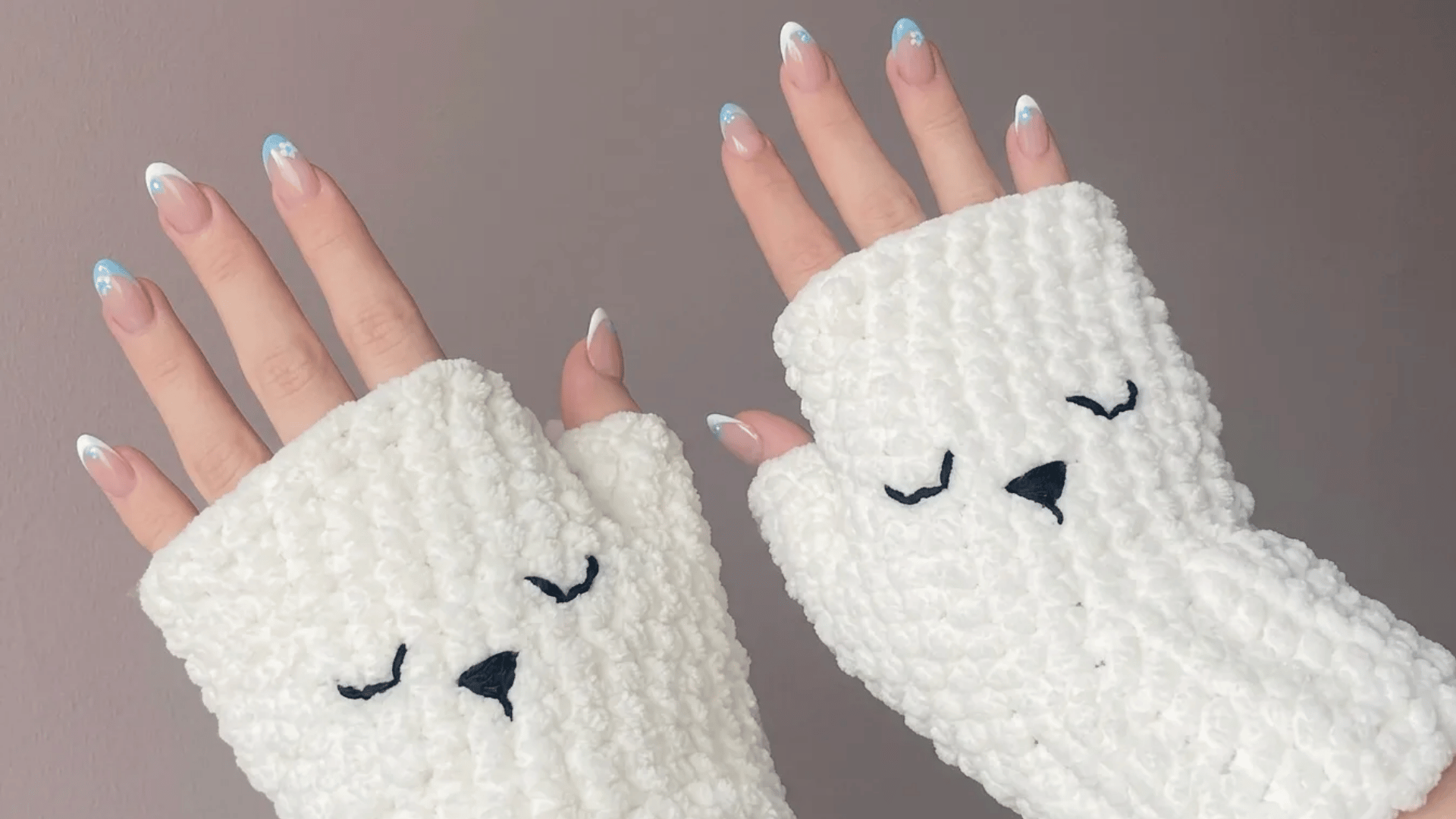 Soft white crochet fingerless gloves with cute embroidered sleepy-face details worn on both hands.