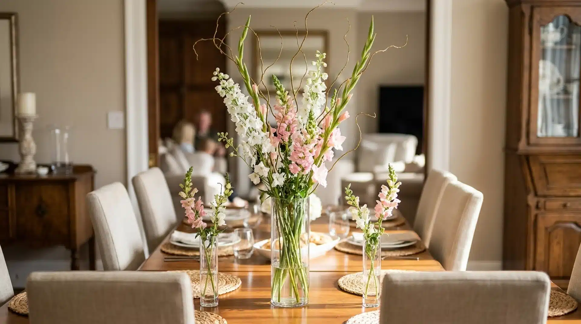 Tall dining table flower arrangement with snapdragons and curly willow in clear glass vases.
