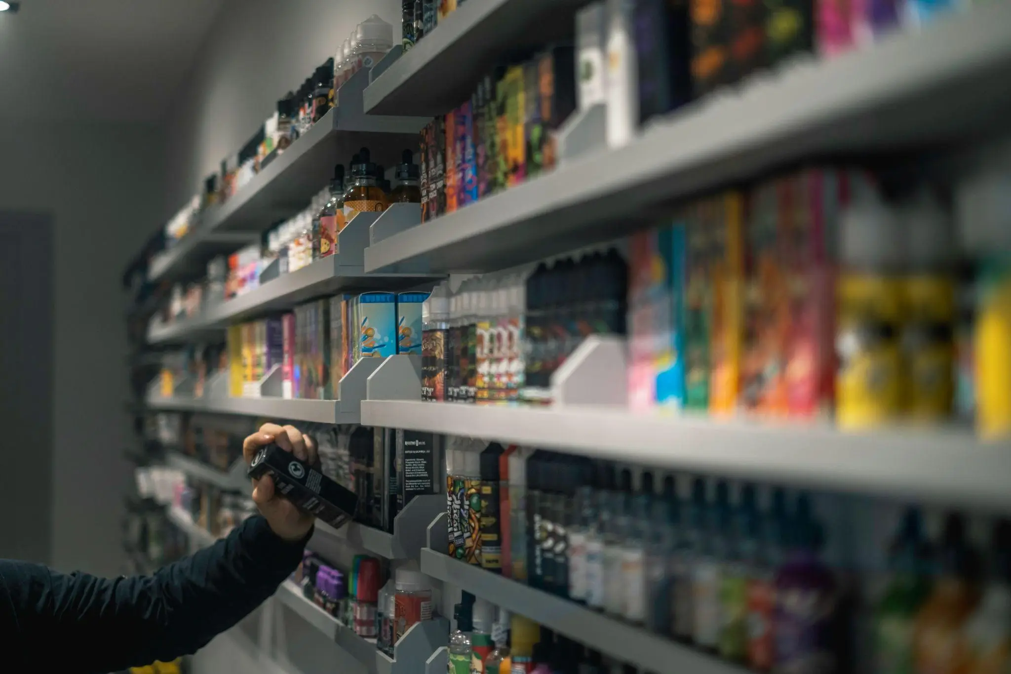 Person selecting a product from shelves filled with colorful e-juice bottles in a vape shop