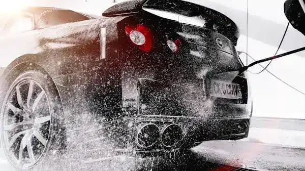 Black sports car being washed with high-pressure water in a car wash station