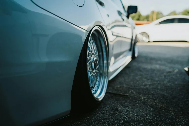 Low-angle view of white car with custom wheels parked on asphalt driveway