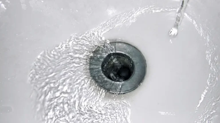 Water swirling down stainless steel sink drain in white bathroom sink