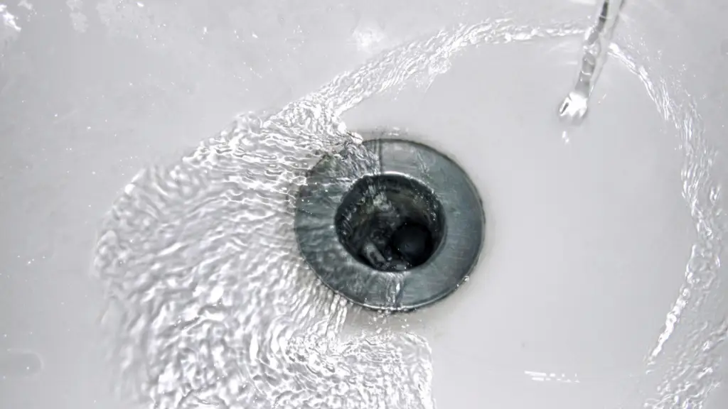 Water swirling down stainless steel sink drain in white bathroom sink
