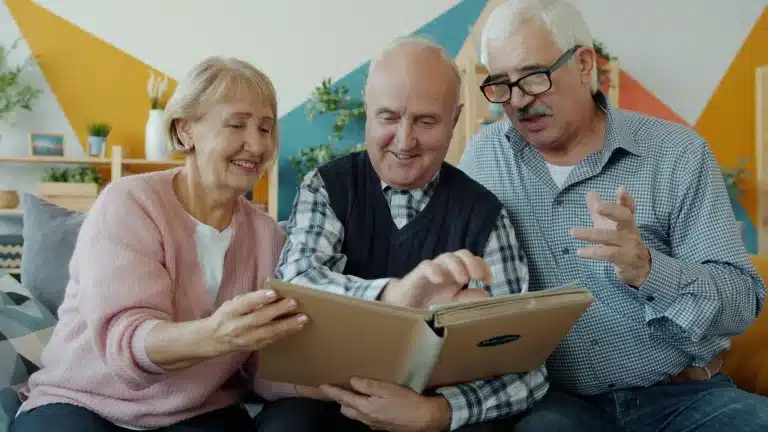 Elderly friends smiling and looking at photo album in colorful living room setting