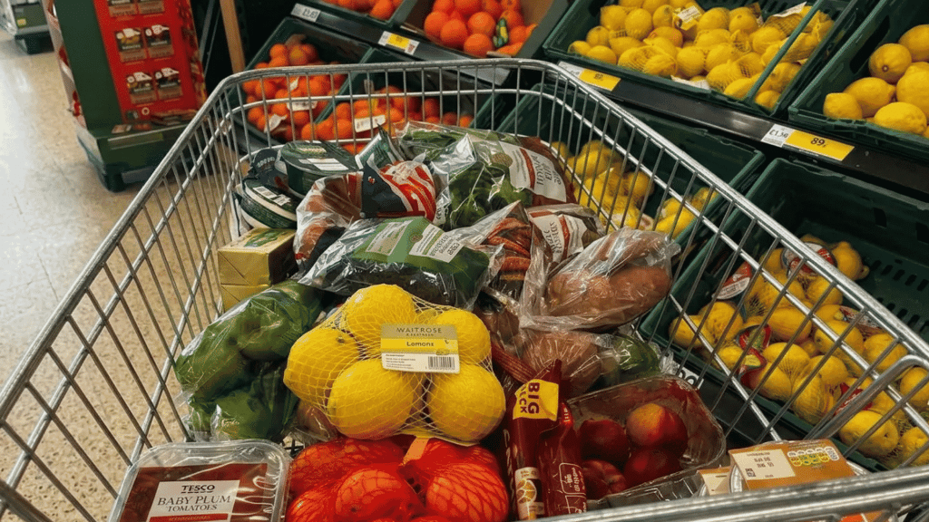 Shopping cart filled with fresh fruits, vegetables, and healthy grocery items inside a supermarket produce section.