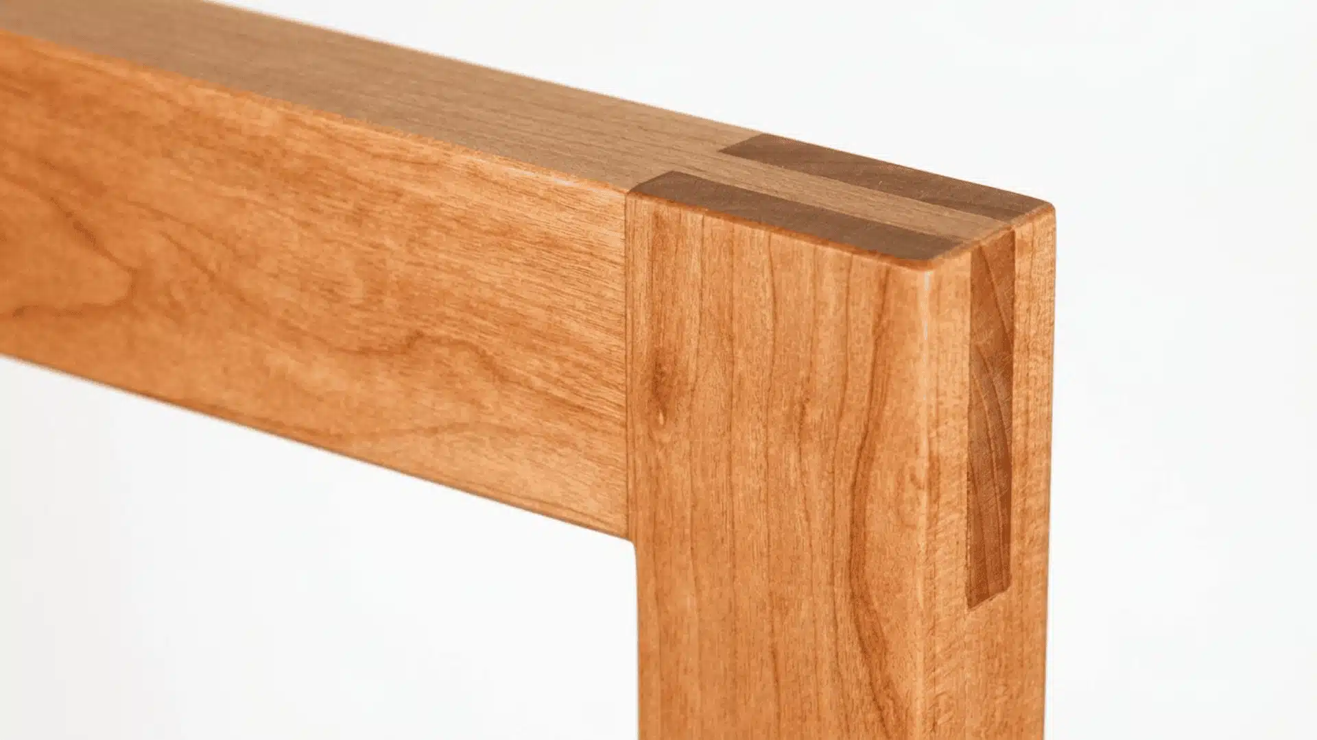 A close-up of a wooden bridle joint connecting two cherry wood beams, showing the interlocking grain and craftsmanship.
