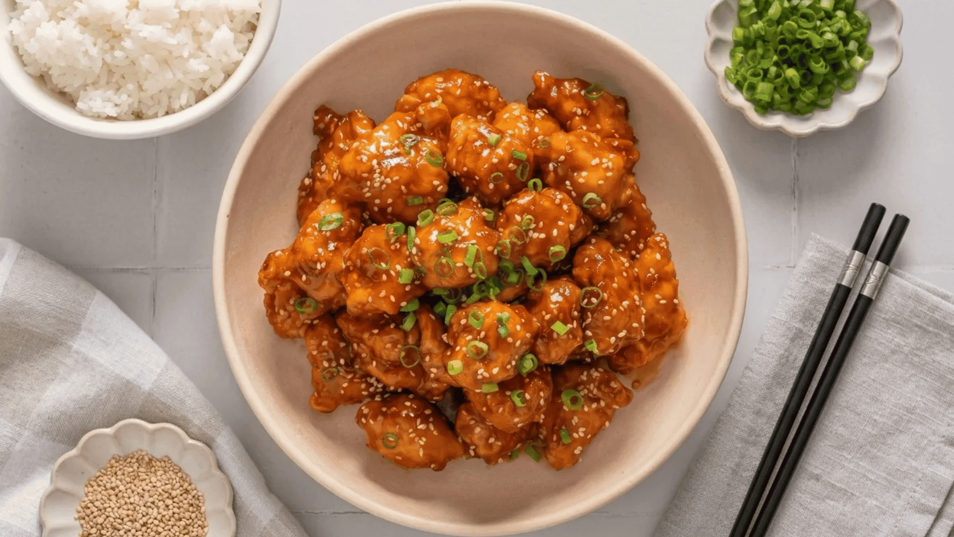 Air fryer orange chicken coated in a sticky citrus sauce with sesame seeds and green onions.