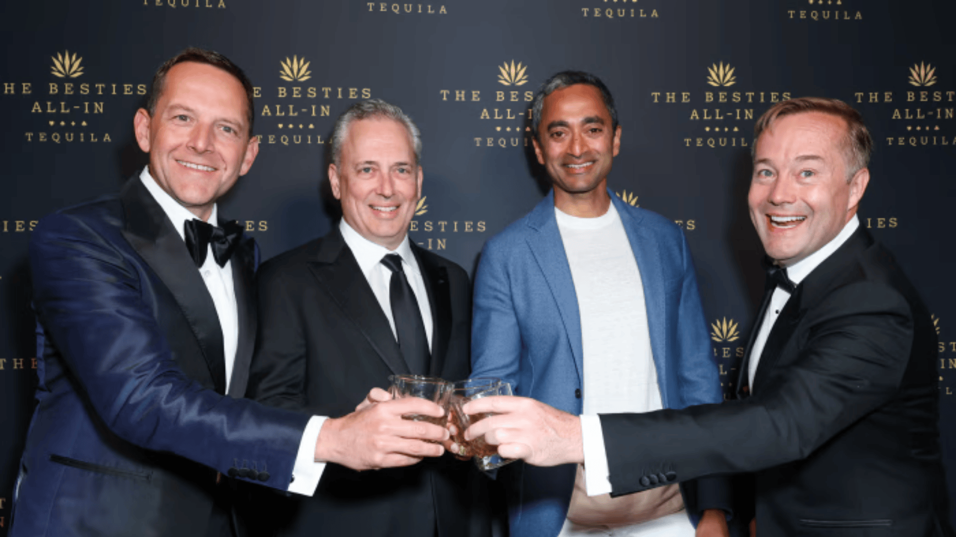 The four All-In Podcast hosts in tuxedos smiling and clinking their glasses together at an evening event.