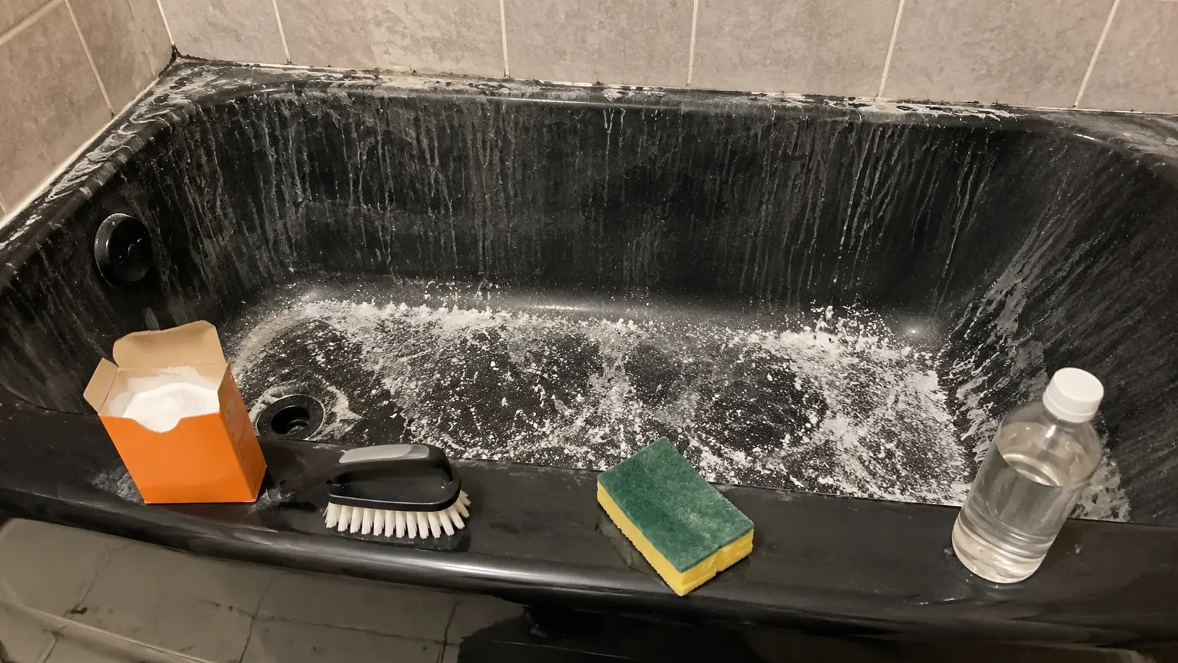 Baking soda and vinegar fizzing in bathtub removing soap scum buildup.