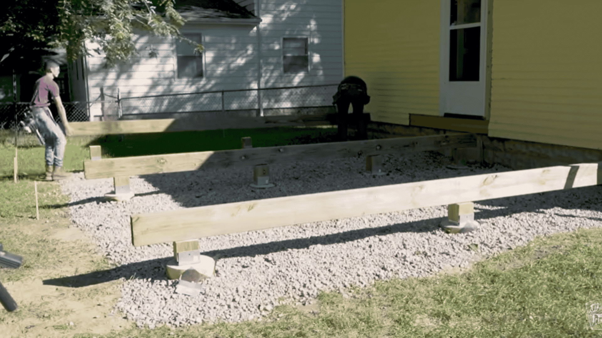 Beams installed on posts with gravel underneath preparing the foundation for a deck