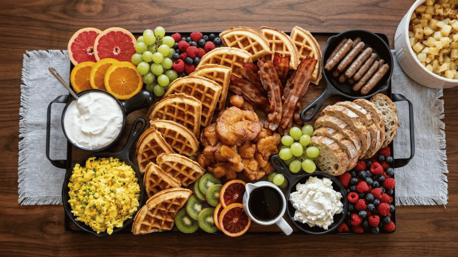 Breakfast-for-dinner board loaded with waffles, eggs, bacon, fruit, sausages, and crispy potatoes for a fun friday night dinner idea.