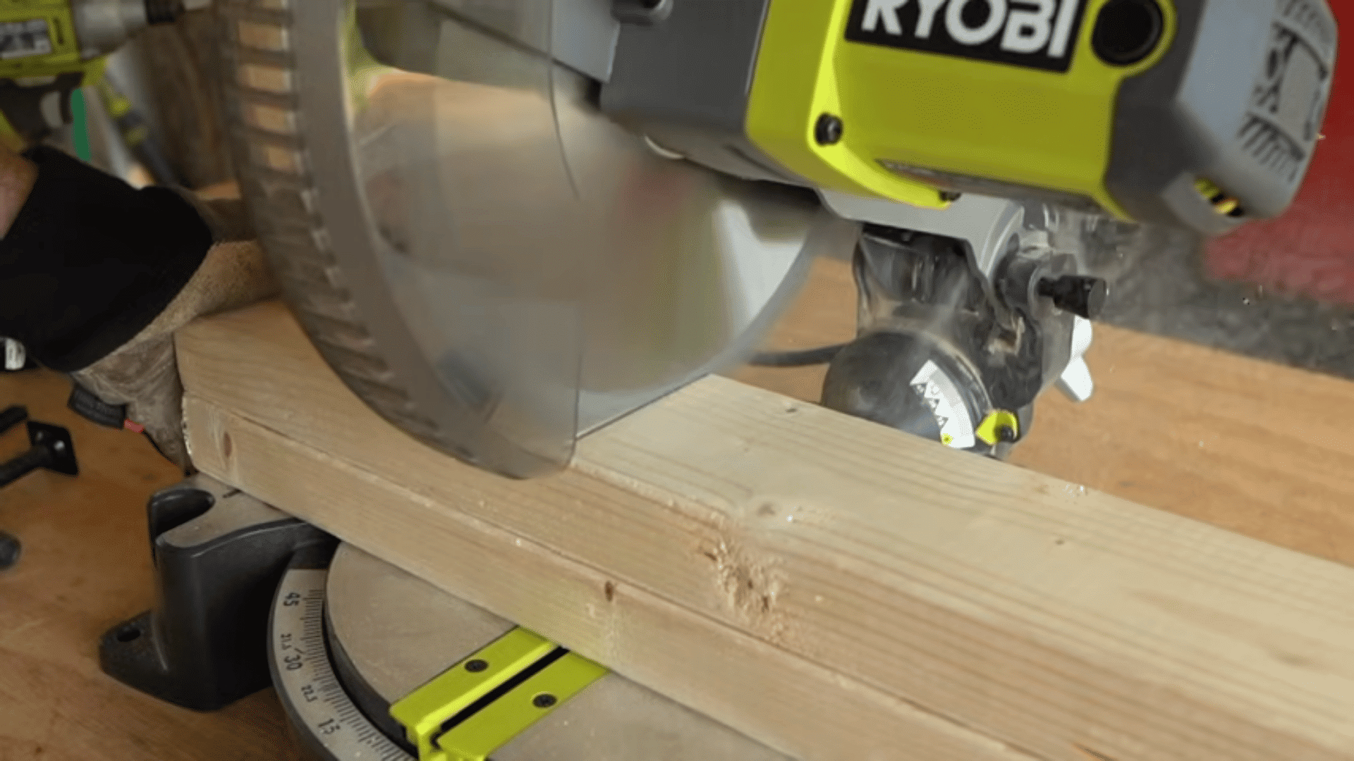 Close-up of a green Ryobi miter saw cutting through a piece of dimensional lumber