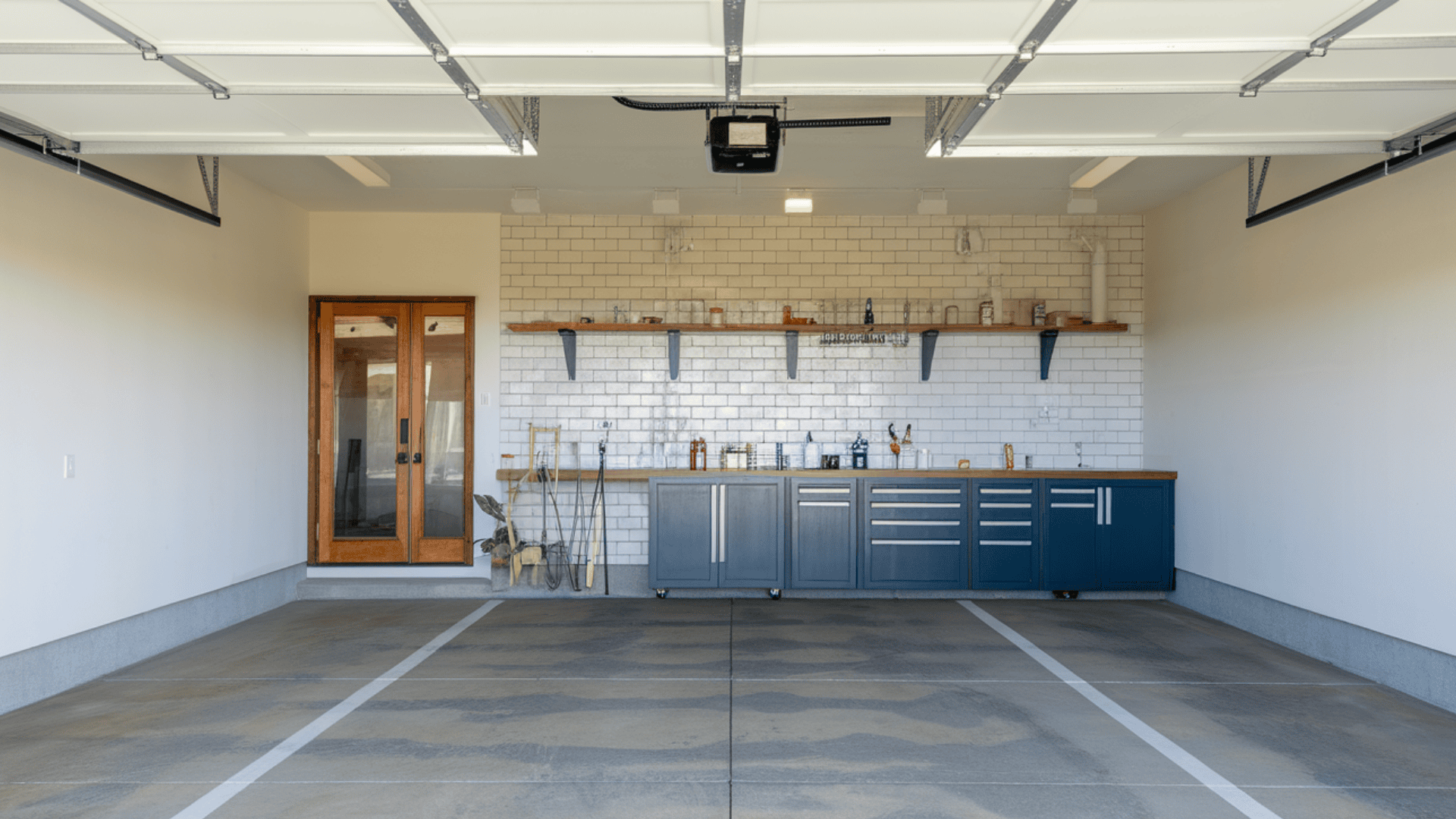 An immaculate garage with a smooth, neutral-toned concrete floor, grey storage cabinets, and warm wood doors.