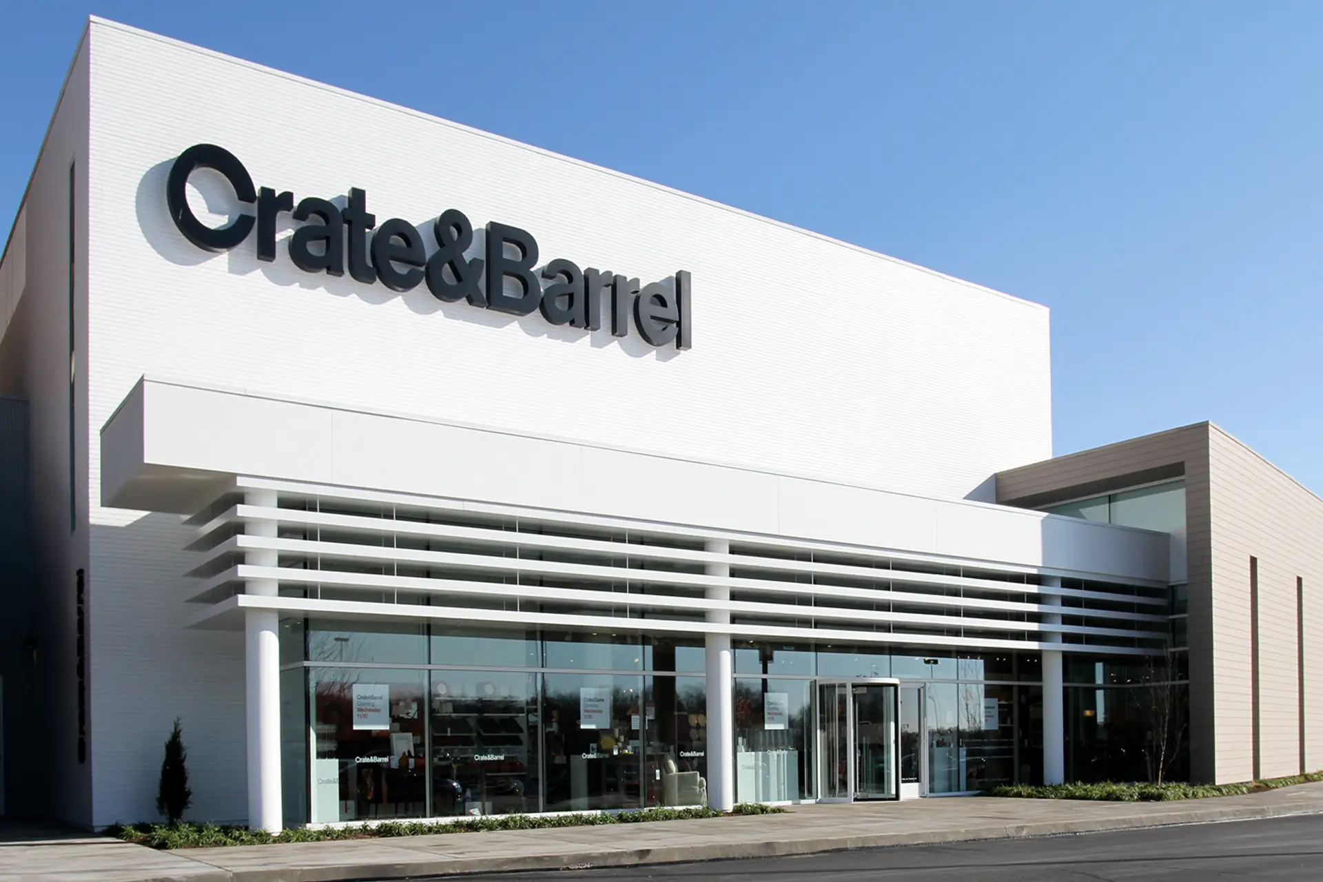 Modern white storefront with large windows and branded signage under clear blue sky