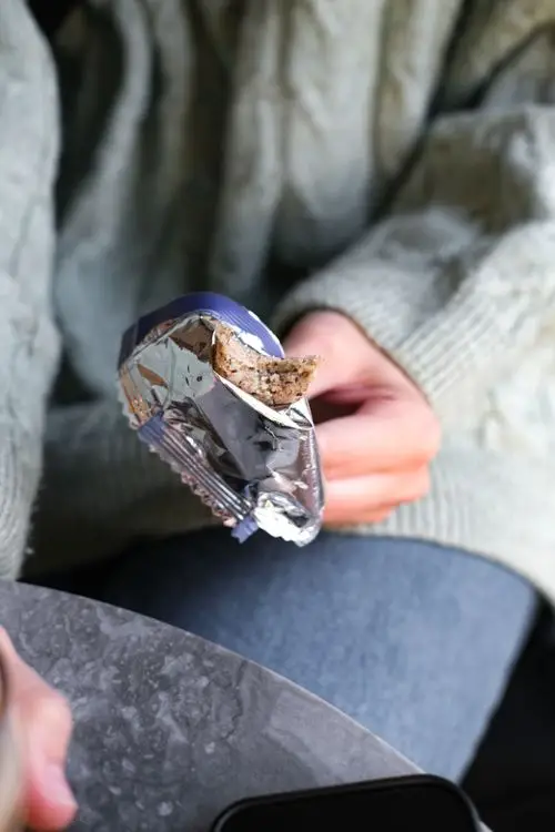 Person holding a partially eaten granola bar in foil wrapper wearing a green sweater