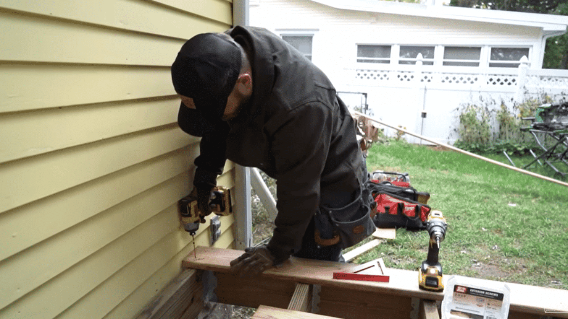 Deck boards being pre-drilled and screwed into the joists near a house for deck installation