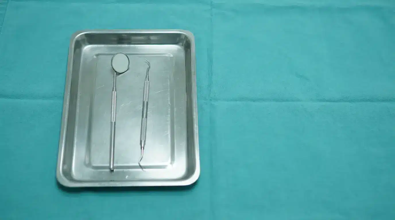 Dental mirror and explorer on stainless steel tray with teal cloth backdrop