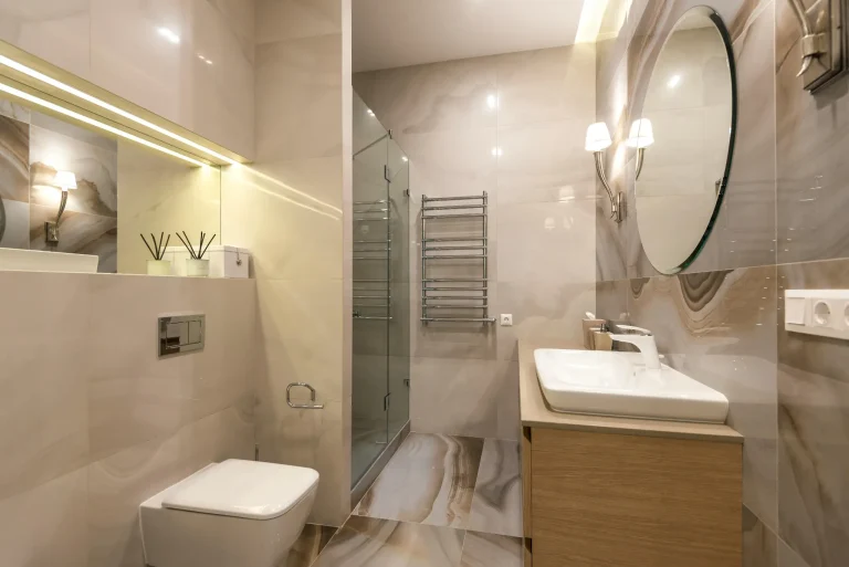 Modern bathroom with glass shower, wooden vanity, and large round mirror under soft lighting