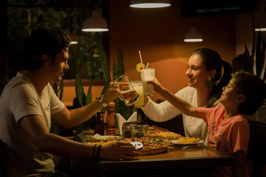Family toasting drinks over pizza in dimly lit restaurant with warm lighting