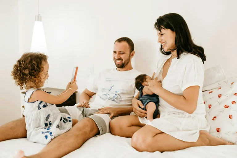 Family sitting on bed in bright room, young child taking a photo with phone