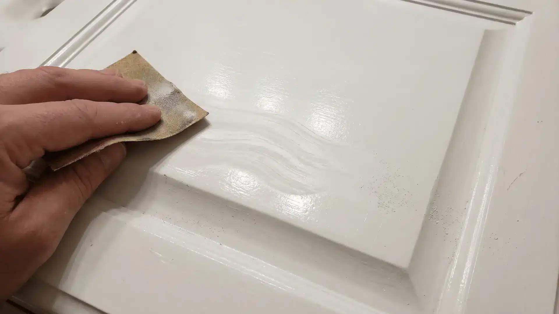 Fine-grit sandpaper lightly sanding glossy bathroom cabinet surface
