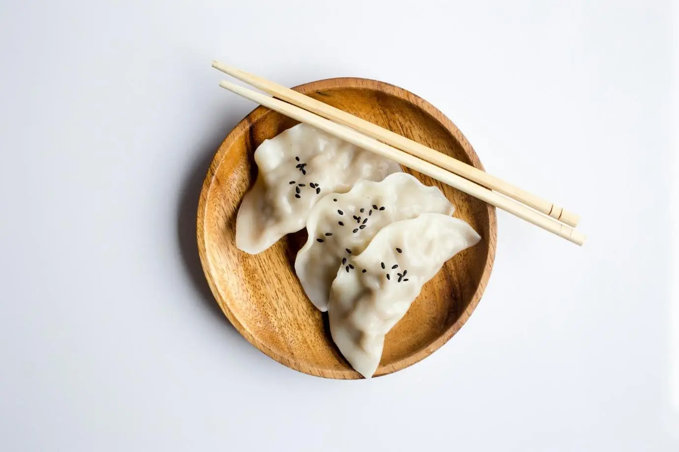 Dumplings with black sesame seeds on a wooden plate with chopsticks on white background