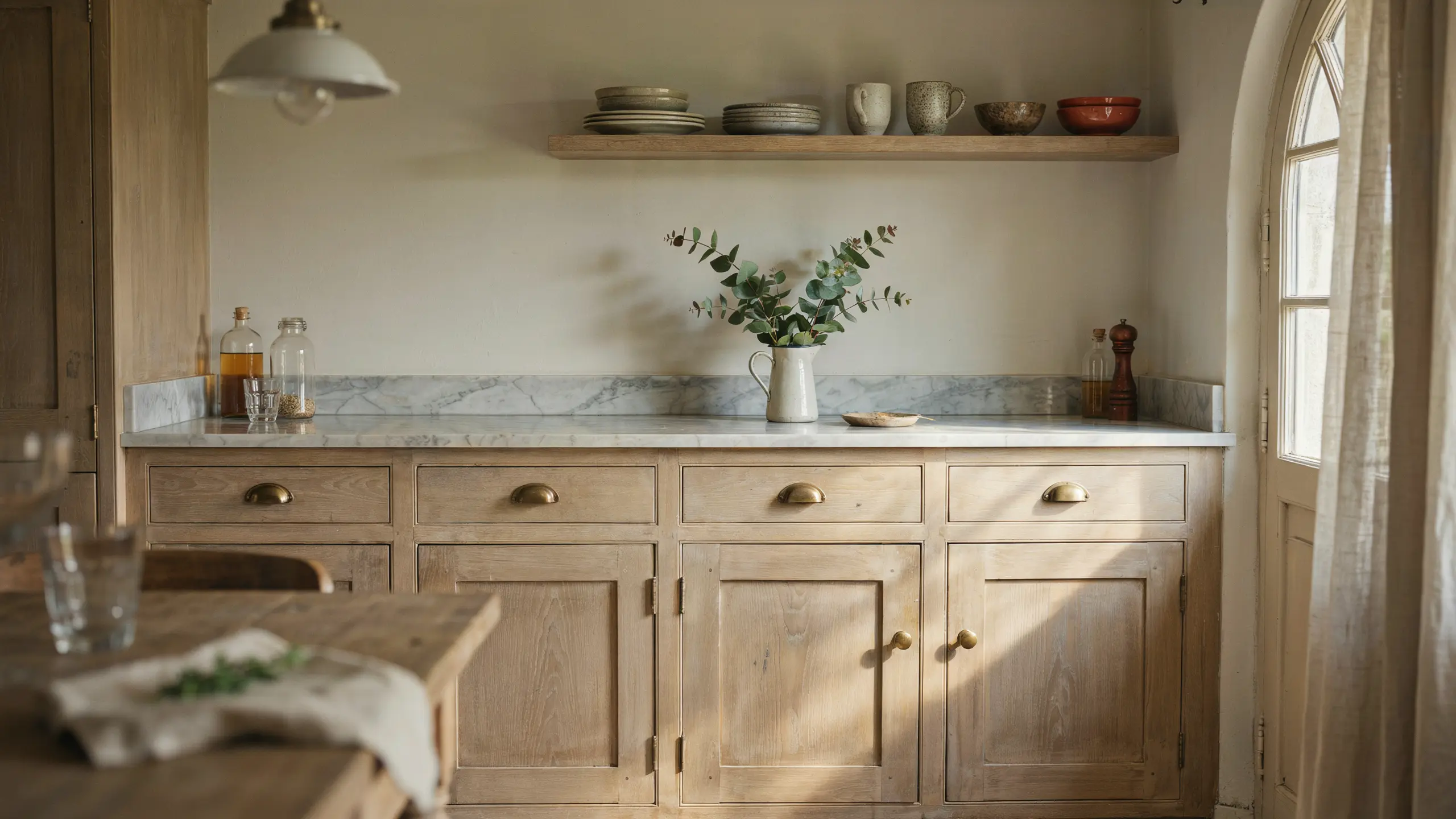 French country kitchen with lightly distressed wood cabinets, cream walls, and marble countertops in a balanced rustic style.