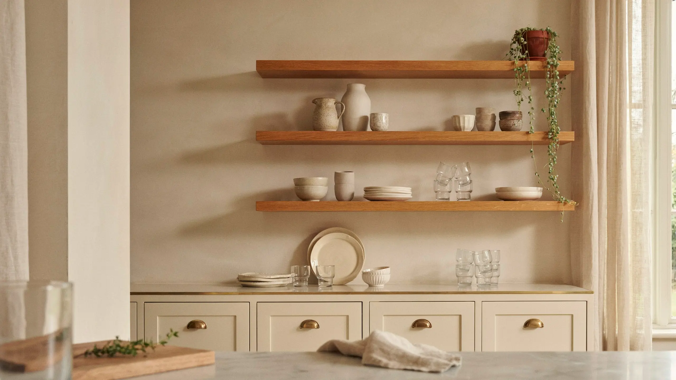 French country kitchen open shelves styled with ceramic dishes, plants, and simple balanced decorative items.