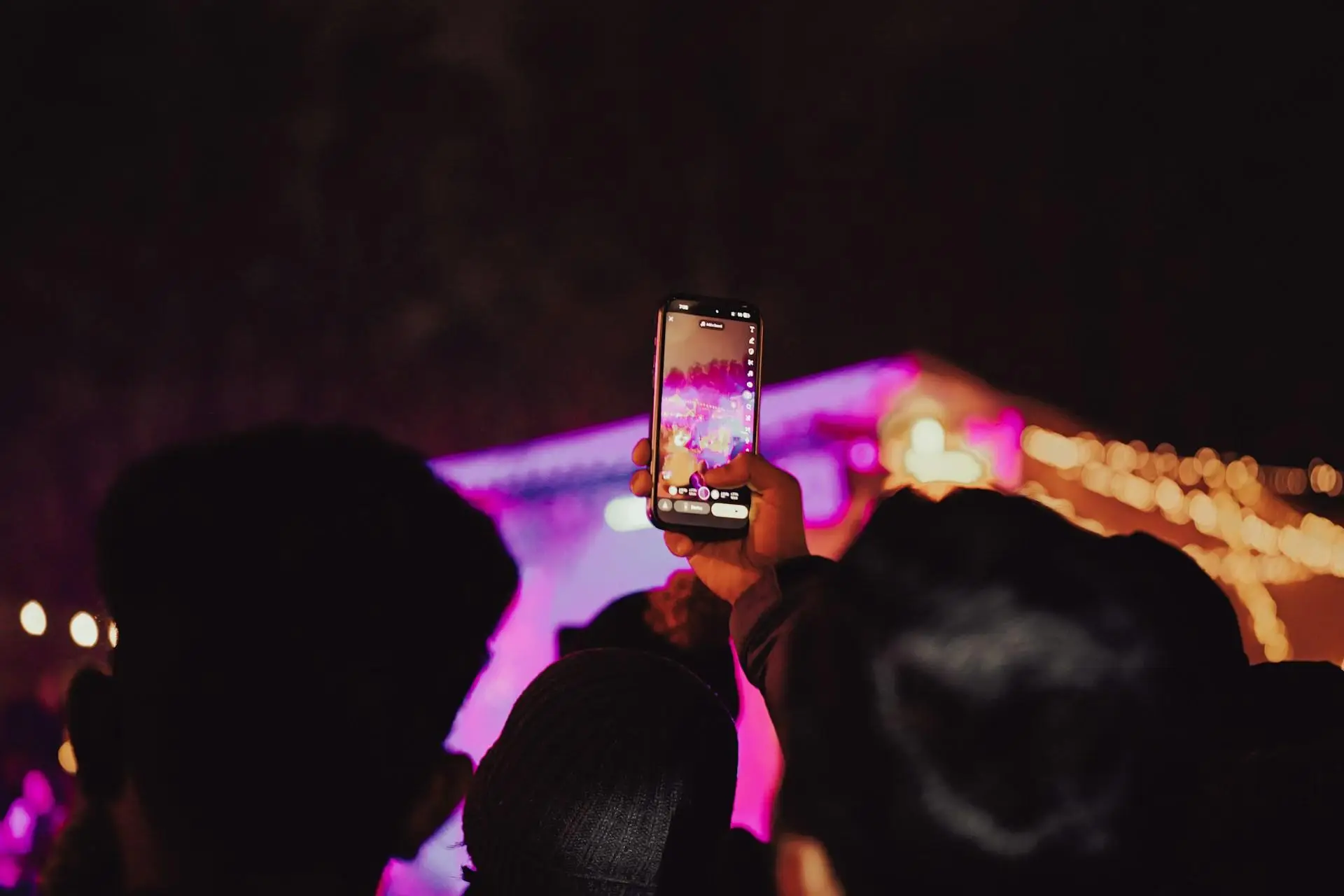 Audience member filming a concert on smartphone during a night performance with colorful stage lights